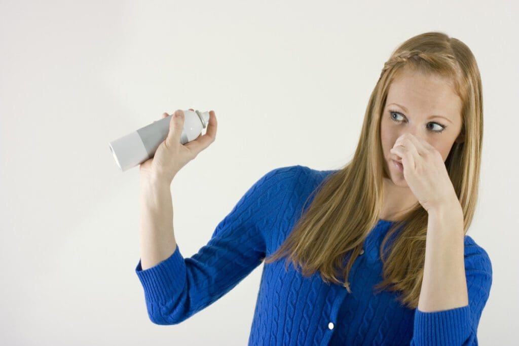 a girl is spraying room freshener with second hand on her nose.