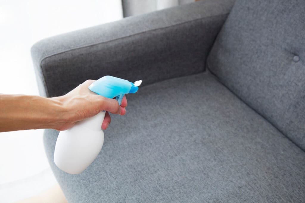 close shot of spray bottle and hand spraying odor eliminator spray on couch.