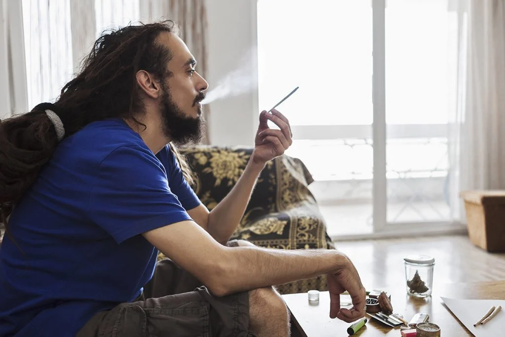 a man sitting on a couch smoking weed in a home.