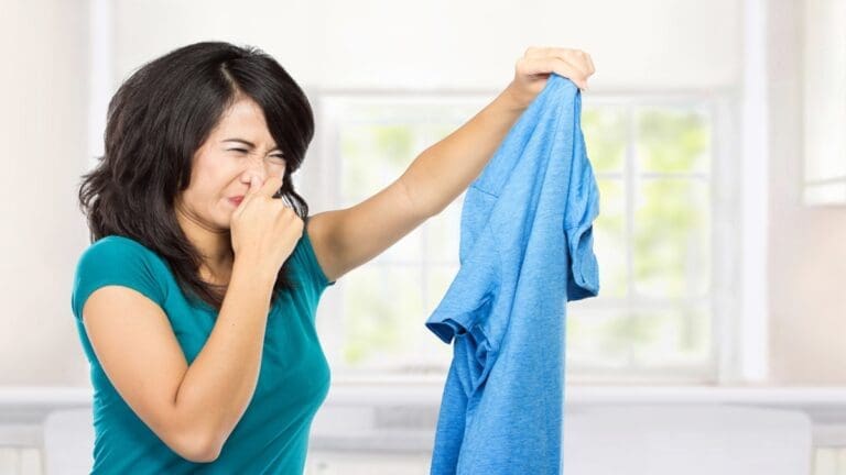 a girl have shirt in her hand and second hand on her nose because of the shirt is smelling bad with smoke odor.