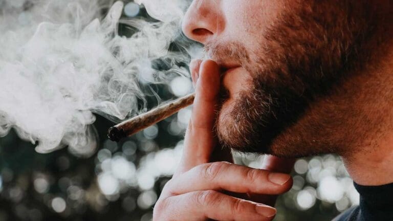 close shot of a man face puffing weed. cloud of smoke can also be seen in picture.