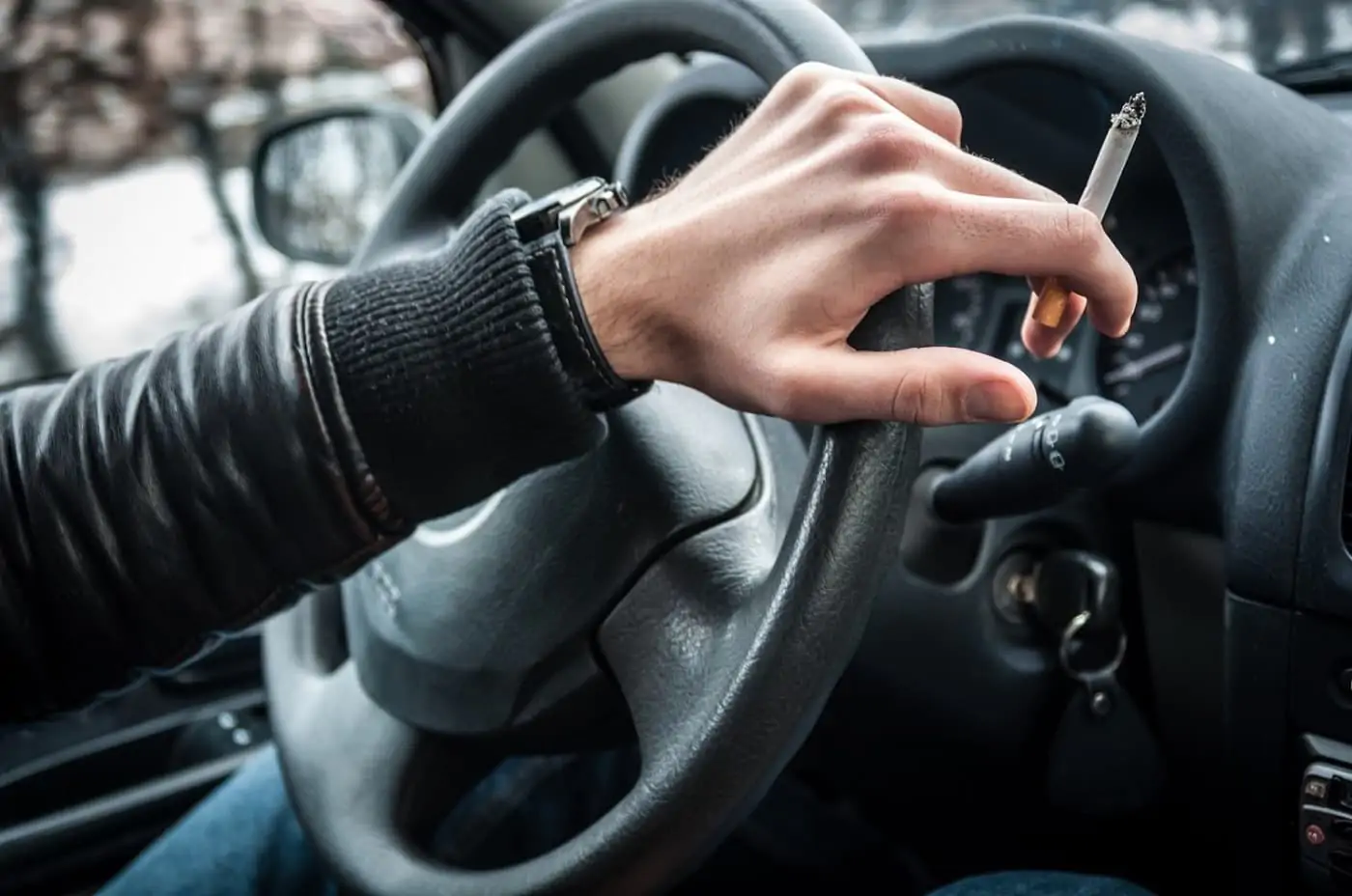 close shot of a hand on steering wheel holding a cigarette.