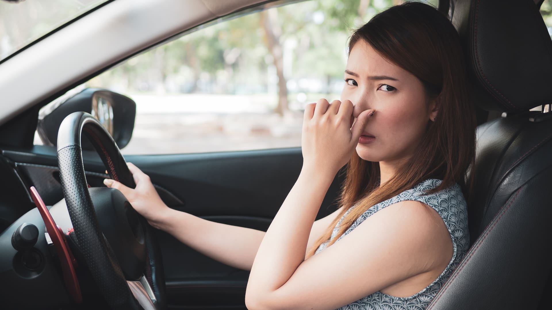 A woman sitting in a car, covering her nose, visibly uncomfortable due to a bad odor inside the vehicle.