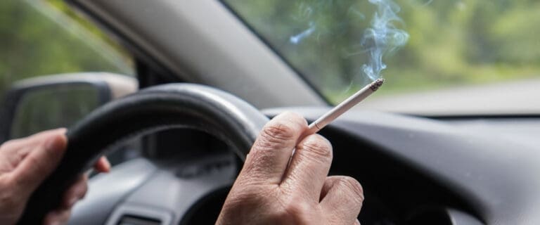 close shot of hands on wheel holding a lighten cigarette in hand.
