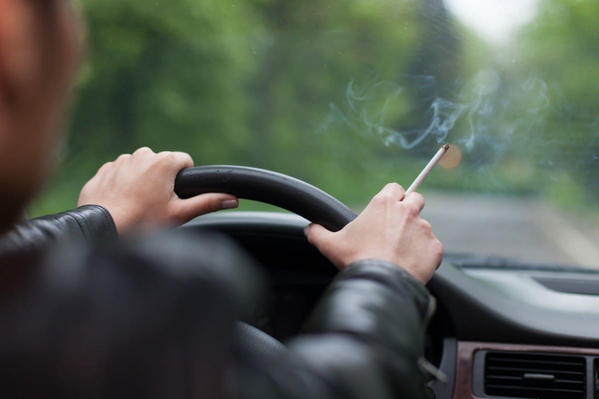 close shot of hands on wheel in the car and holding a cigarette in hand.