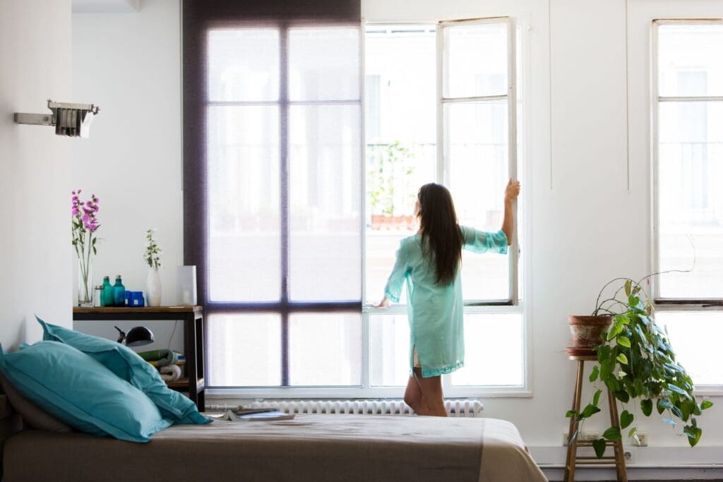 a woman opening window and a fresh home can be seen in picture.